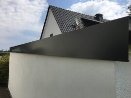Graue Blende an der Dachkante eines Gebäudes mit einem hellen Wandbereich.