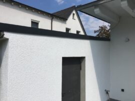 Weiße Wand mit grauem Dach und einer dunklen Tür in einem Wohnbereich.