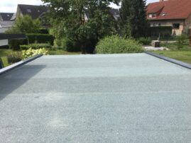 Flachdach mit grauer Beschichtung auf einem Garagengebäude in einer Wohngegend.