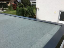 Flachdach mit grauer Abdichtung und Metallrand an einem Garagengebäude.