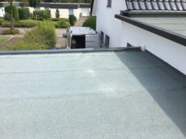 Flachdach mit grauer Beschichtung und einem Lieferwagen im Hintergrund.