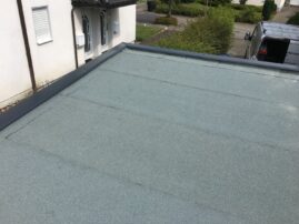 Flachdach mit grauer Beschichtung und mehreren Fugen auf der Oberfläche.