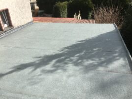 Flachdach einer Garage mit grauer Oberfläche und Schattenwurf von Bäumen.