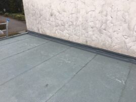 Flachdach mit grauer Abdichtung und strukturierten Wänden im Hintergrund.