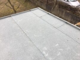 Flachdach mit grauer Oberfläche und sichtbaren Rissen in der Beschichtung.
