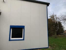 Seitenansicht eines Gebäudes mit grauer Fassade und einem blauen Fensterrahmen.
