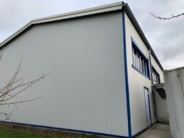 Grau-blaues Industriegebäude mit einer schrägen Wand und mehreren Fenstern.