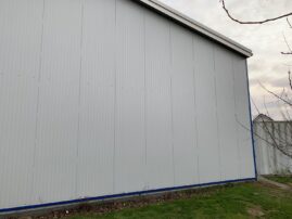 Graue Wand eines Gebäudes mit vertikalen Metallpaneelen und einem blauen Rand am Boden.