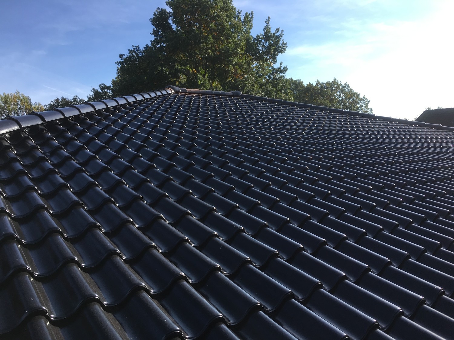 Schwarzes Dach mit glatten Dachziegeln, das in der Sonne glänzt.