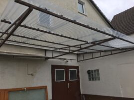 Transparente Wellenplattenüberdachung über einem Eingang mit Metallrahmen.