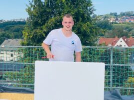Ein Mann hält eine Dämmplatte auf einem Dach, während er auf einer Baustelle steht.