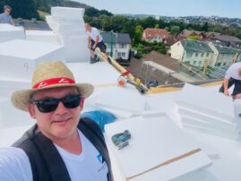 Dachdecker auf einem Flachdach, umgeben von Dämmmaterialien und Werkzeugen.