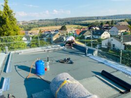 Arbeiter auf einem Flachdach, das mit Bitumenbahnen und einer Dachbegrünung ausgestattet ist.