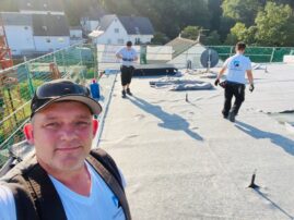 Zwei Dachdecker arbeiten auf einem Flachdach mit Bitumenbahnen und Dachbegrünung.